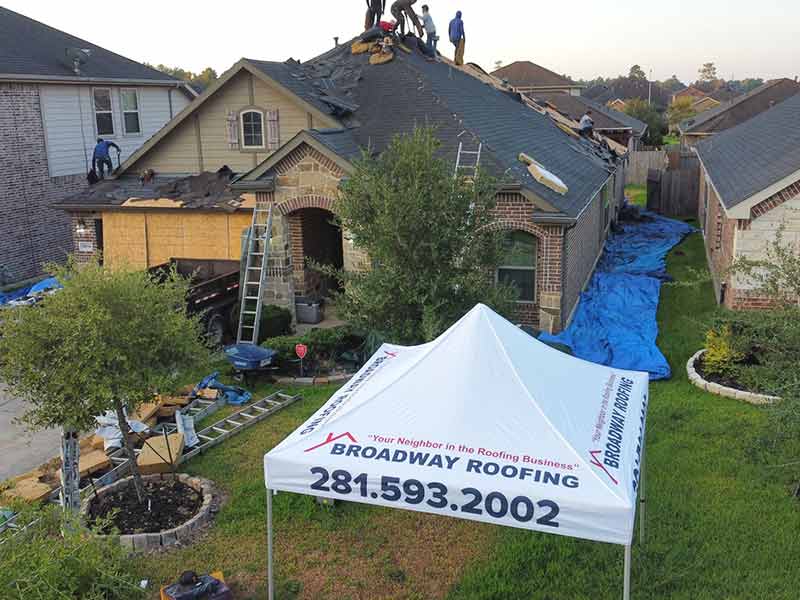 Broadway Roofing working on a residential roof replacement with their tent on the front yard