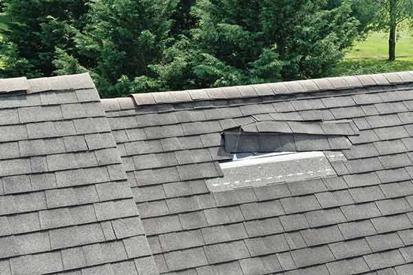 Residential roof with some gray shingles falling off due to storm damage